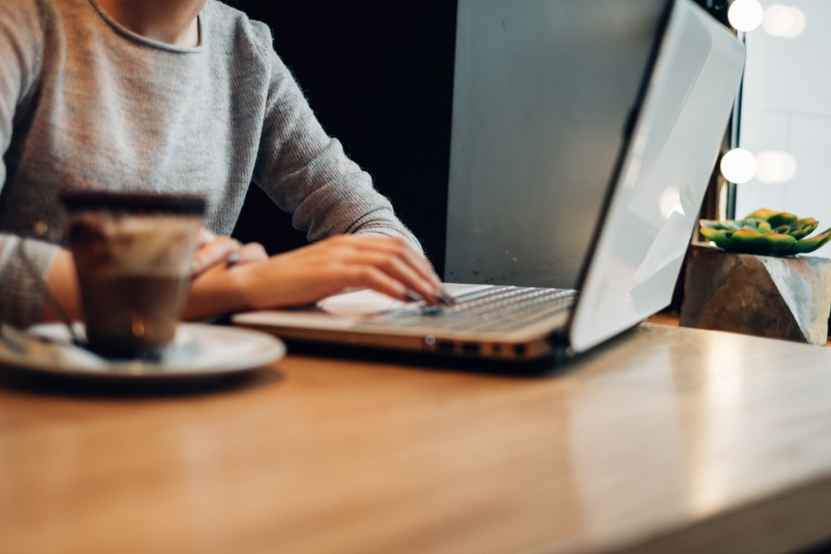 Personne travaillant sur un ordinateur portable dans un café, illustrant l'utilisation des outils d'intelligence artificielle pour rédiger des articles dans le cadre d'une stratégie webmarketing.